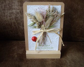 Wooden stand with a handmade paper card and a bunch of dried flowers