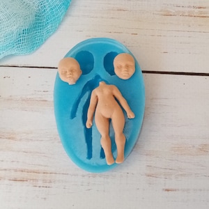May include: A blue silicone mould for making doll figures. The mould has two separate cavities, one for the body and one for the head. The mould is on a white wooden surface.