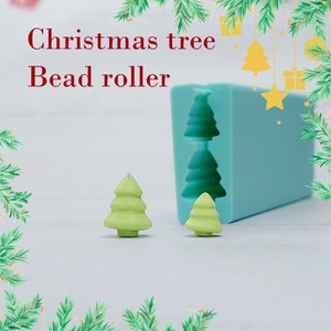 Peut inclure: Un rouleau à perles en forme de sapin de Noël vert clair avec deux petites perles en forme de sapin de Noël vertes. Un moule bleu avec des formes de sapin de Noël est en arrière-plan. Le texte "Christmas tree Bead roller" est en haut de l'image.