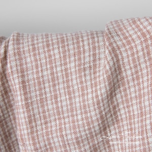May include: Close-up of folded fabric with a small, checkered pattern. The fabric is a blend of white and a muted rose colour, creating a textured appearance. The weave is visible, suggesting a linen or similar material.