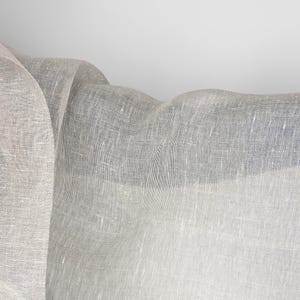 May include: A white sheer fabric with a textured weave. The fabric is draped and folded, creating soft folds and curves.