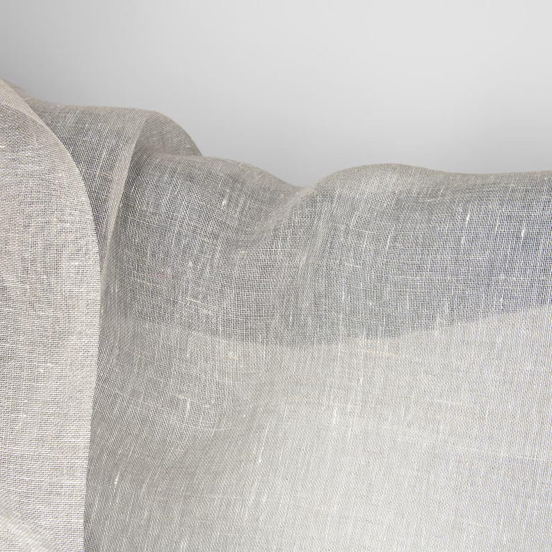 May include: A white sheer fabric with a textured weave. The fabric is draped and folded, creating soft folds and curves.