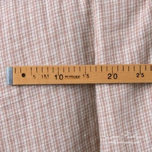 May include: A close-up shot of a fabric with a light brown and white checkered design. A wooden ruler, marked in centimetres, lies across the fabric. The ruler has black markings and the text "TURHAN". The website address "www.linenfashion.com" is visible.
