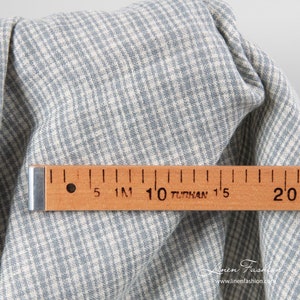 May include: Close-up of a blue and white checkered fabric with a wooden ruler. The fabric is folded, showing the texture and pattern. The ruler measures up to 20 inches, with the text "TUNHAN" visible.