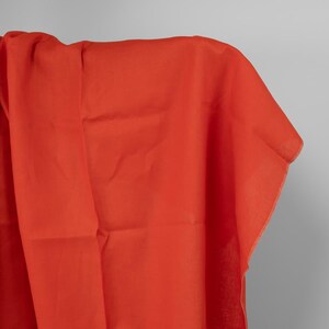 Può includere: Un tessuto arancione vibrante drappeggiato su un'asta. Il tessuto è di colore uniforme, con pieghe e pieghe visibili, che suggeriscono un materiale leggero. I bordi del tessuto sono visibili, mostrando un orlo pulito e rifinito. L'aspetto generale è liscio e fluido.