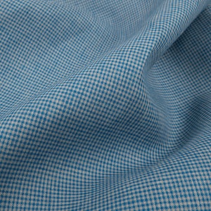 May include: Close-up of a blue and white gingham fabric. The fabric is folded, showing the texture and pattern of the woven material. The pattern is a classic small check design, suitable for various sewing projects.