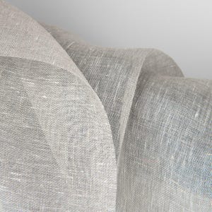 May include: Close-up of a piece of light gray linen fabric with a textured weave. The fabric is folded and draped, creating soft folds and curves.