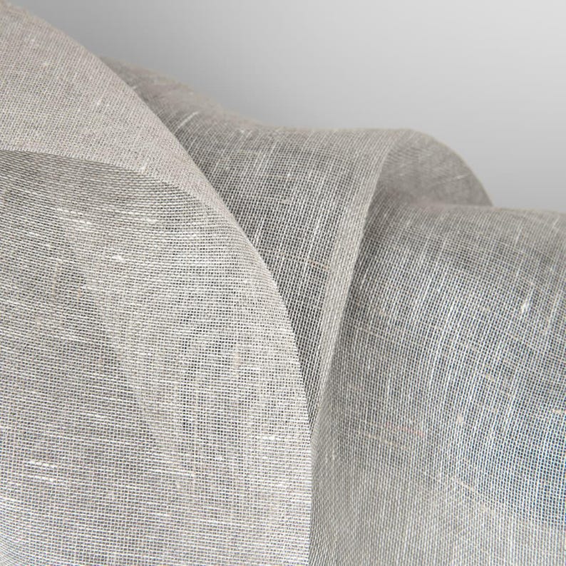 May include: Close-up of a piece of light gray linen fabric with a textured weave. The fabric is folded and draped, creating soft folds and curves.