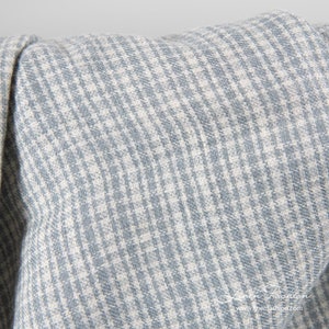 May include: Close-up of a blue and white houndstooth pattern fabric. The fabric is folded, showing the texture and weave of the material. The pattern is a classic design, with small, repeating checks.
