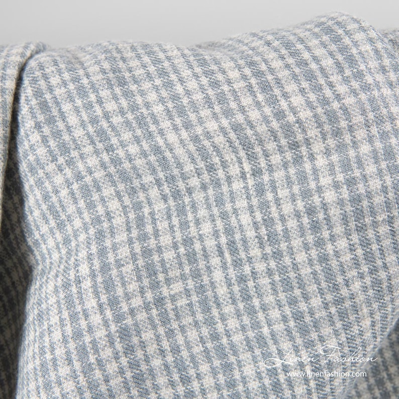 May include: Close-up of a blue and white houndstooth pattern fabric. The fabric is folded, showing the texture and weave of the material. The pattern is a classic design, with small, repeating checks.