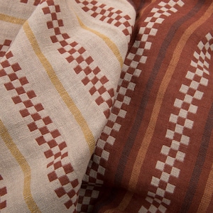 Könnte beinhalten: Nahaufnahme eines gewebten Stoffes mit einem karierten Muster in Braun- und Beigetönen. Der Stoff ist gefaltet und texturiert und zeigt die komplizierten Details der Webart.