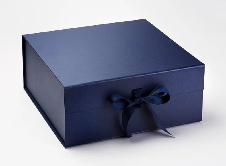 Puede incluir: Una caja de regalo azul marino con una cinta de sat&eacute;n atada en un lazo. La caja est&aacute; hecha de cart&oacute;n resistente y tiene un acabado liso y mate.