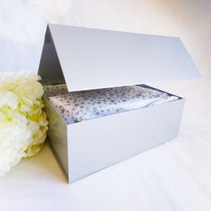 May include: A white gift box with a lid that is open. The box is lined with white tissue paper with a silver star pattern.