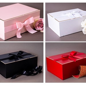 Può includere: Quattro scatole regalo con coperchi e nastri di diversi colori. Le scatole sono rosa, bianca, nera e rossa. Ogni scatola ha un bordo dorato.