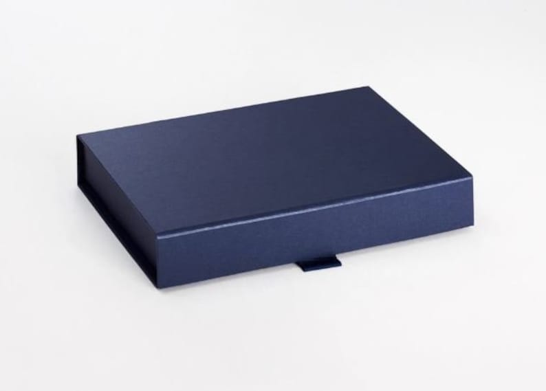 May include: A navy blue rectangular gift box with a magnetic closure. The box is made of a textured material and has a small tab on the front for opening. The box is sitting on a white surface.
