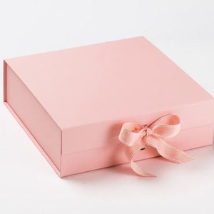Peut inclure: Une boîte cadeau rose pâle avec un ruban de satin rose assorti noué en un nœud.