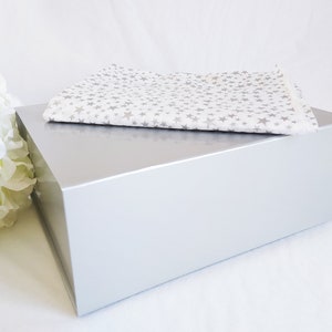 May include: A silver gift box with a white tissue paper with a silver star pattern on top.