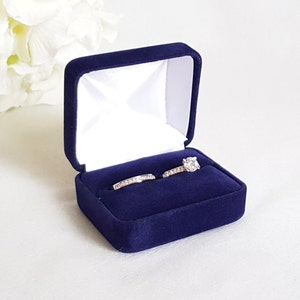 May include: A navy blue velvet ring box containing two rings. The larger ring features a single large diamond, while the smaller ring has a band of smaller diamonds.