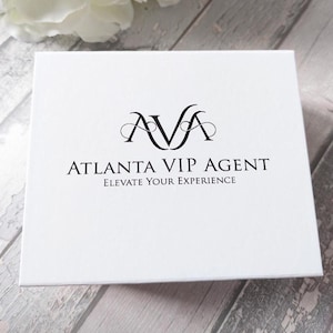May include: A white box with the text "AVA ATLANTA VIP AGENT ELEVATE YOUR EXPERIENCE" in black. The box has a logo with the letters "AVA" in a stylized font. The background is a light gray wood-grain pattern.