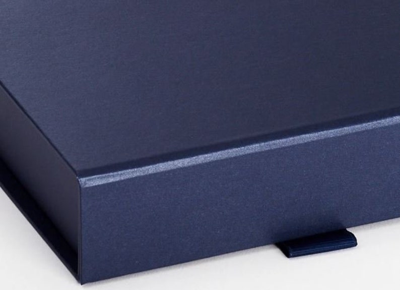 May include: A close-up of a navy blue box with a textured surface. The box has a matching navy blue ribbon pull. The box is likely for packaging or storage.