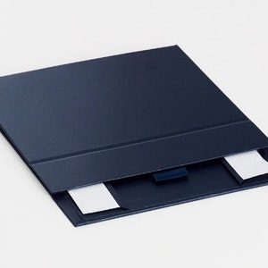 May include: A navy blue presentation folder with a textured finish. The folder is open, revealing two white notecards. A dark blue ribbon is attached to the inside of the folder.