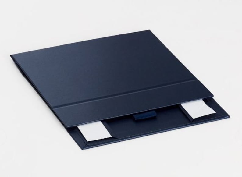 May include: A navy blue presentation folder with a textured finish. The folder is open, revealing two white notecards. A dark blue ribbon is attached to the inside of the folder.