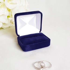 May include: A blue velvet ring box with a white satin interior. Two silver rings with a single diamond are sitting outside the box.