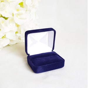 May include: A small, dark blue velvet ring box with a white interior. The box is open and empty.