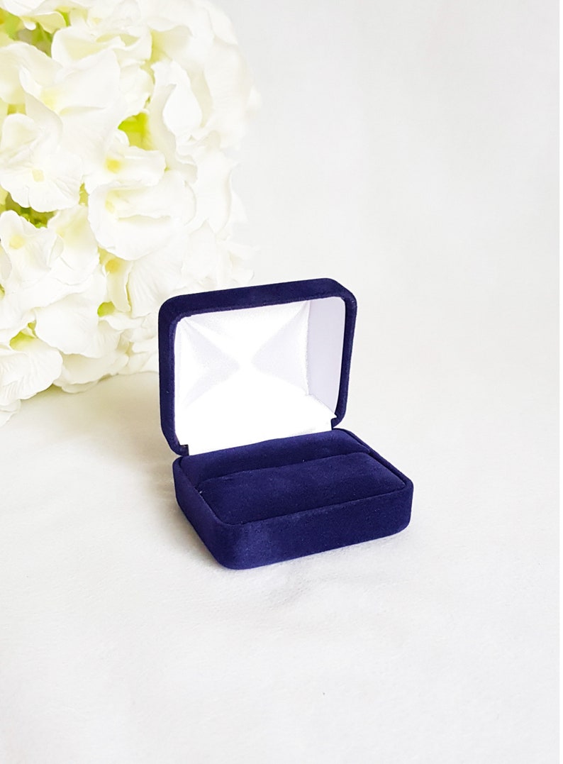 May include: A small, dark blue velvet ring box with a white interior. The box is open and empty.