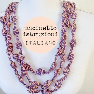 May include: A multi-strand necklace made of crocheted yarn with purple and peach colored knots. The necklace is on a white mannequin. The text "uncinetto istruzioni italiano" is written in a circle on the image.