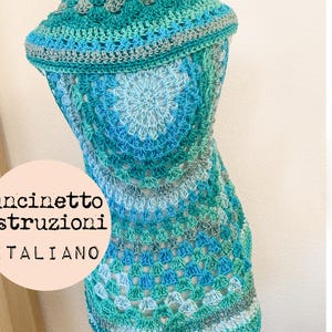 May include: A crocheted top in shades of blue and green, with a scalloped edge. The top is displayed on a white mannequin. The text "uncinetto istruzioni ITALIANO" is visible on a pink circle.
