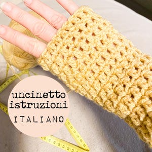 May include: A close-up of a yellow crocheted fingerless glove. The glove is being held by a hand. The text "uncinetto istruzioni ITALIANO" is visible in the image.