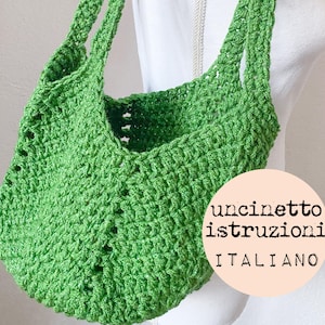 May include: A green crocheted tote bag with a double strap. The bag is made with a simple stitch pattern and has a slightly slouchy shape. The text "uncinetto istruzioni italiano" is written on a pink circle.