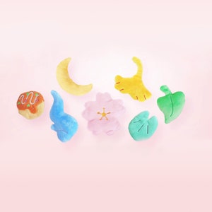 Puede incluir: Un conjunto de ocho juguetes de peluche de diferentes formas y colores, que incluyen una luna creciente, una flor, una hoja, una nube, un takoyaki y una hoja de ginkgo. Los juguetes son todos suaves y tiernos y ser&iacute;an perfectos para la habitaci&oacute;n o la sala de juegos de un ni&ntilde;o.