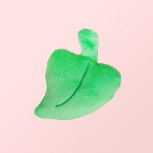 Puede incluir: Un juguete de peluche verde en forma de hoja con una l&iacute;nea cosida en el centro.