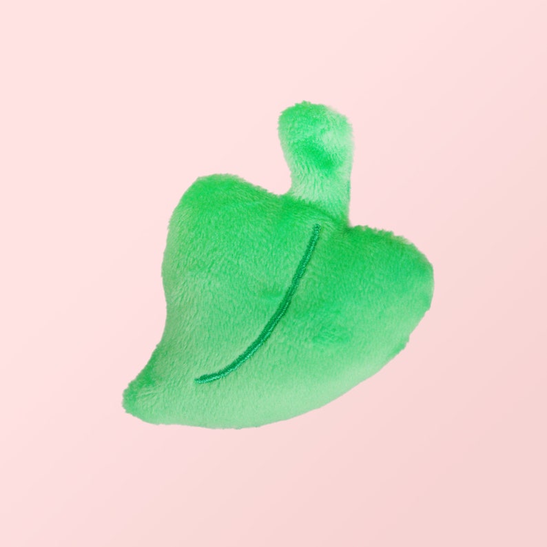 Puede incluir: Un juguete de peluche verde en forma de hoja con una l&iacute;nea cosida en el centro.