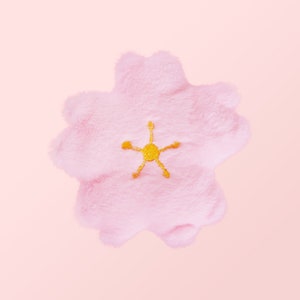 Puede incluir: Una flor de felpa rosa suave con una estrella amarilla bordada en el centro.