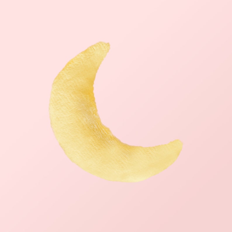 Puede incluir: Una forma de media luna amarilla hecha de material suave y peludo sobre un fondo rosa.