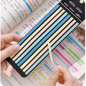 May include: A set of colorful sticky strips for marking pages in a book. The strips are in various pastel colors, including pink, blue, yellow, and green. The strips are labeled "sticky strips book home office".