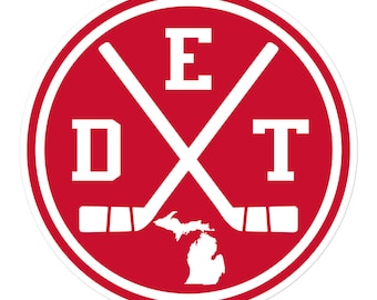 May include: Red and white circular sticker with the letters "D" and "T" on either side of a pair of crossed hockey sticks with the letter "E" above them. The sticks are topped with blades and the state of Michigan is in the center of the sticker.