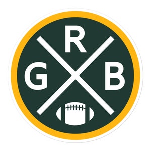 May include: Circular sticker with a green background, a yellow border, and white text and accents. The letters "G", "R", and "B" are displayed in white, with a white football graphic at the bottom. The letters are intersected by white lines.