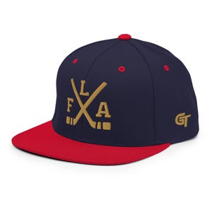 Könnte beinhalten: Eine marineblaue Snapback-Cap mit flachem rotem Schirm und rotem Knopf oben. Die Vorderseite zeigt goldfarben gestickte gekreuzte Hockeyschläger mit den Buchstaben F, L und A. Die Seite zeigt ein goldenes GT-Logo und rote Ösenakzente.