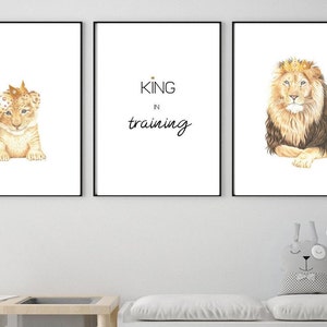 May include: A triptych of framed art prints with lion imagery. One shows a lion cub with a crown, another reads "KING in training", and the last depicts a lion wearing a crown. The prints are in black frames.