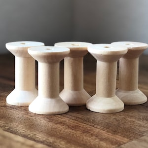 May include: Five wooden spools, all the same size and shape, are arranged in a row on a wooden surface. The spools are a light natural wood color.