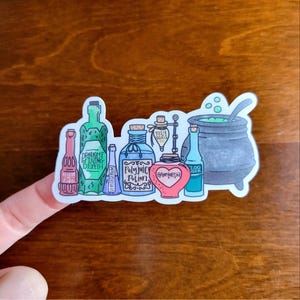 May include: A sticker featuring various potion bottles and a cauldron. The bottles are labeled with names like "Draught of Living Death" and "Polyjuice Potion." The cauldron has green liquid and a spoon.