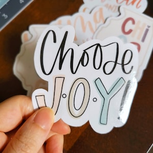 May include: A white sticker with the text "Choose Joy!" in black script. The word "Joy" is in colorful outlined letters.