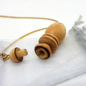 Op de afbeelding: Een houten slinger met een gouden ketting en een kleine houten stop. De slinger zit in een witte gaas zak.