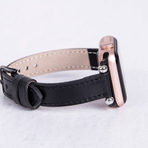 Puede incluir: Una correa de reloj de cuero negro con un Apple Watch de oro rosa.