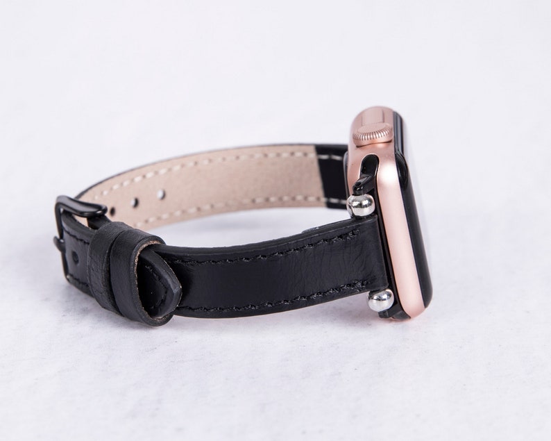 Puede incluir: Una correa de reloj de cuero negro con un Apple Watch de oro rosa.