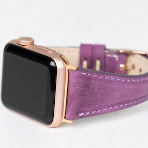 May include: A rose gold Apple Watch with a purple leather band. The watch face is black and the band has white stitching.